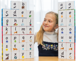 Child sitting at table with lowercase tile toppers stacked up on magnetic tiles and she is looking and smiling at them. 