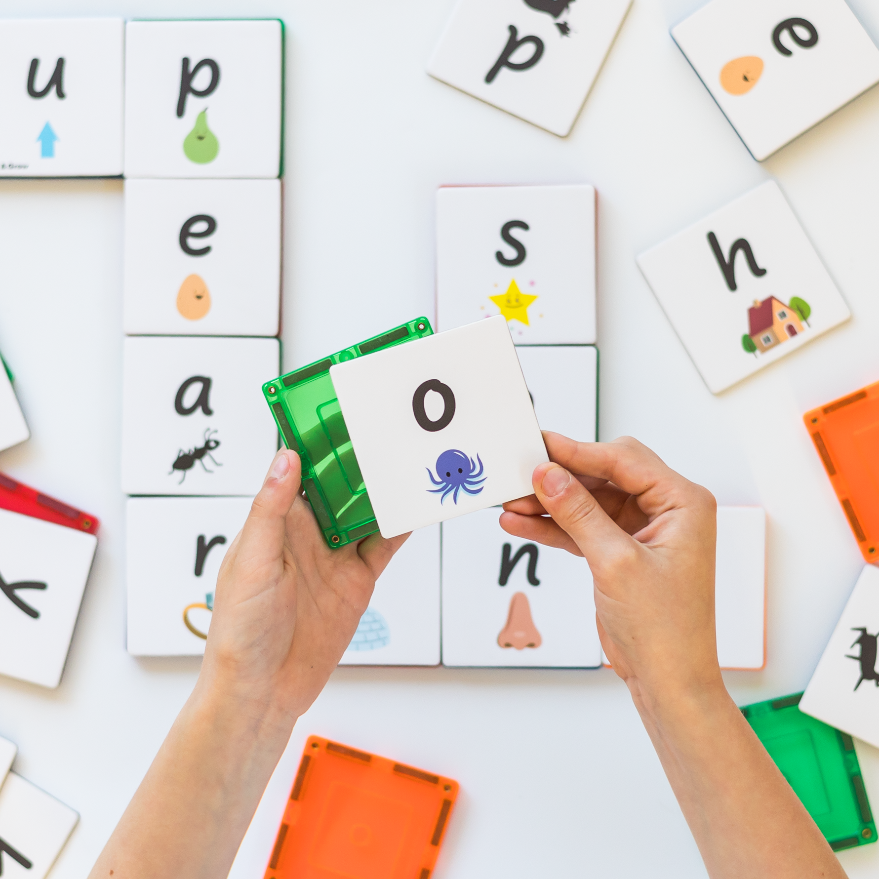 Hands showing putting an lowercase o tile topper onto a green magnetic tile