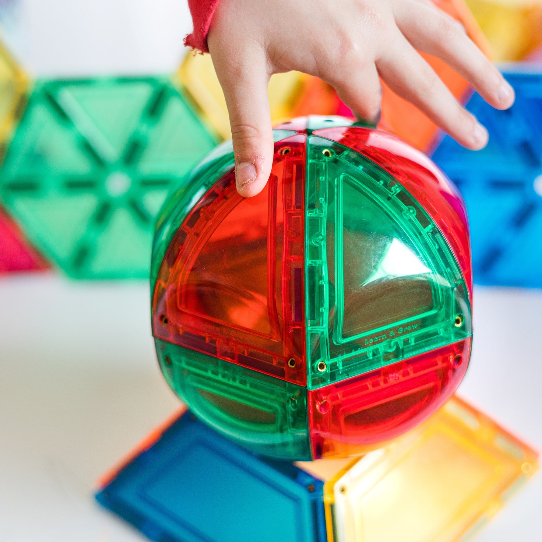 Child touching red and green shiny magnetic tile dome on stand 