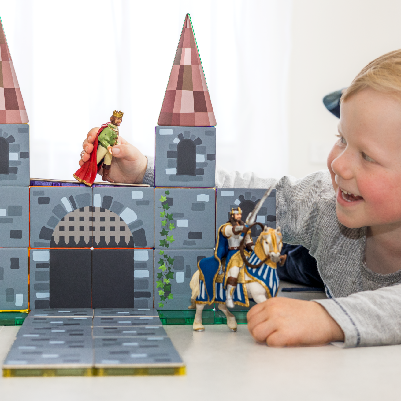 Boy playing with a castle made from magnetic tile toppers & holding knights in his hand