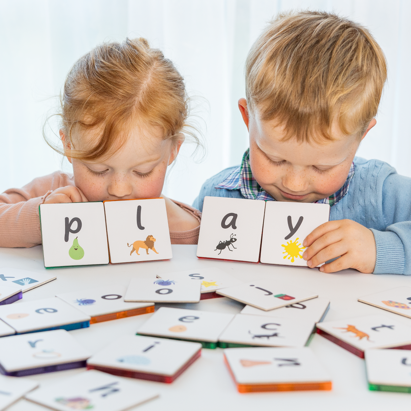 2 kids looking down at lowercase letters that are tile toppers stuck to a magnetic tile